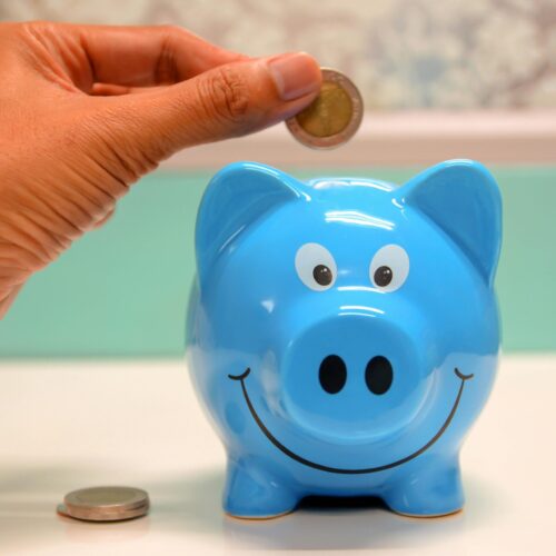 Hand inserting a coin into a blue piggy bank for savings and money management.