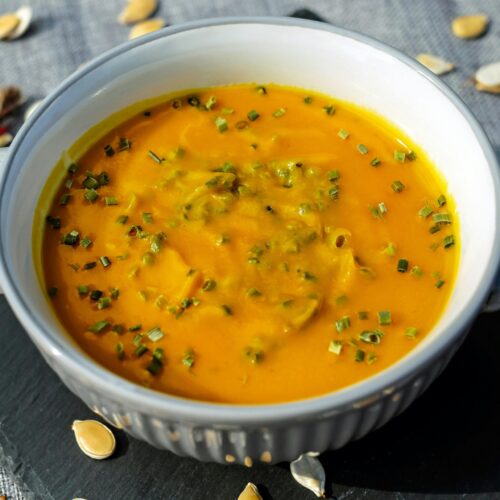 Warm and creamy pumpkin soup garnished with fresh herbs, perfect for a cozy meal.