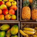Colorful display of apples, pineapples, bananas, and papayas in wooden crates at a market.
