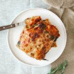 Tasty homemade Italian lasagna served on a rustic setting with rosemary garnish.