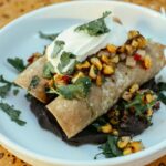 Close-up of enchiladas topped with corn salsa and sour cream, beautifully plated.