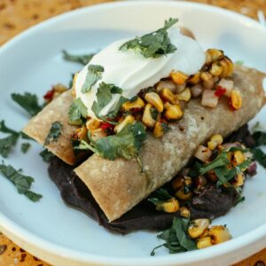 Close-up of enchiladas topped with corn salsa and sour cream, beautifully plated.