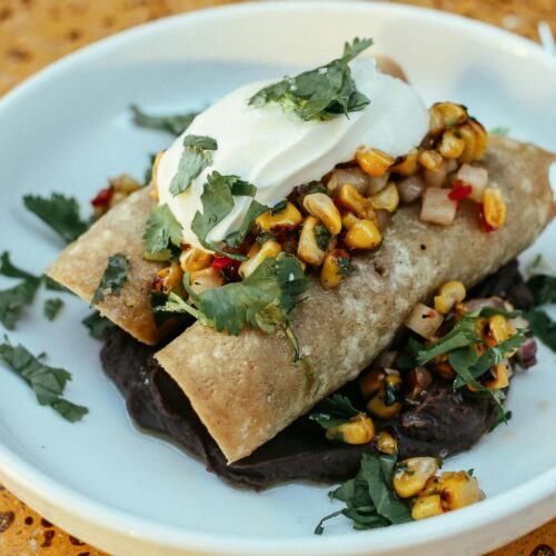 Close-up of enchiladas topped with corn salsa and sour cream, beautifully plated.