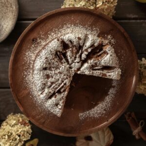 Rustic flat lay of a sliced cake with powdered sugar on a wooden table, perfect for dessert inspiration.