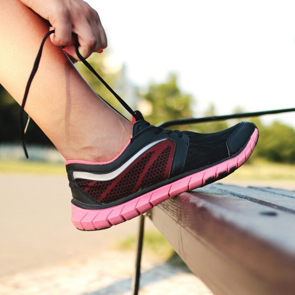 A woman laces her sneakers on a park bench, preparing for a run outdoors.