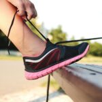 A woman laces her sneakers on a park bench, preparing for a run outdoors.