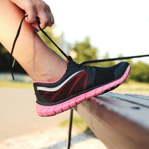 A woman laces her sneakers on a park bench, preparing for a run outdoors.