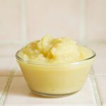 Close-up of homemade applesauce in a clear glass bowl on a tiled surface.