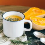 A cozy setting with butternut squash soup in a mug, complemented by fresh ingredients and rustic decor.