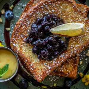 Tasty French toast topped with blueberry compote and a lemon slice, served with a side of custard.