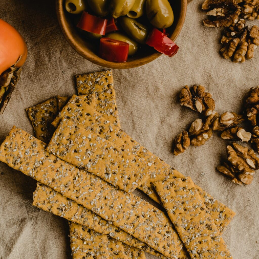 Flat lay of crackers, walnuts, and olives on a cloth, perfect for a rustic snack board theme.