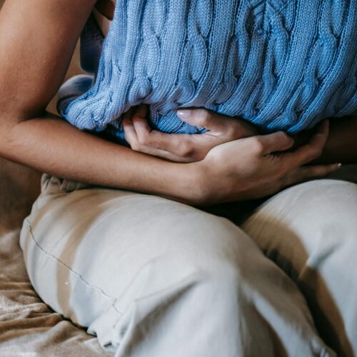 Crop unrecognizable female touching belly while having acute pain in stomach sitting on couch