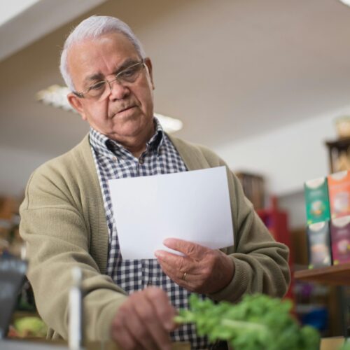 Elderly man shopping in a Portuguese grocery store, holding a paper list.
