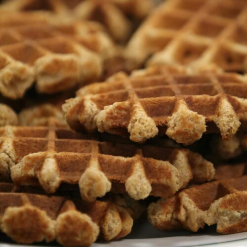 A stack of golden homemade waffles served on a white plate, ready to enjoy.